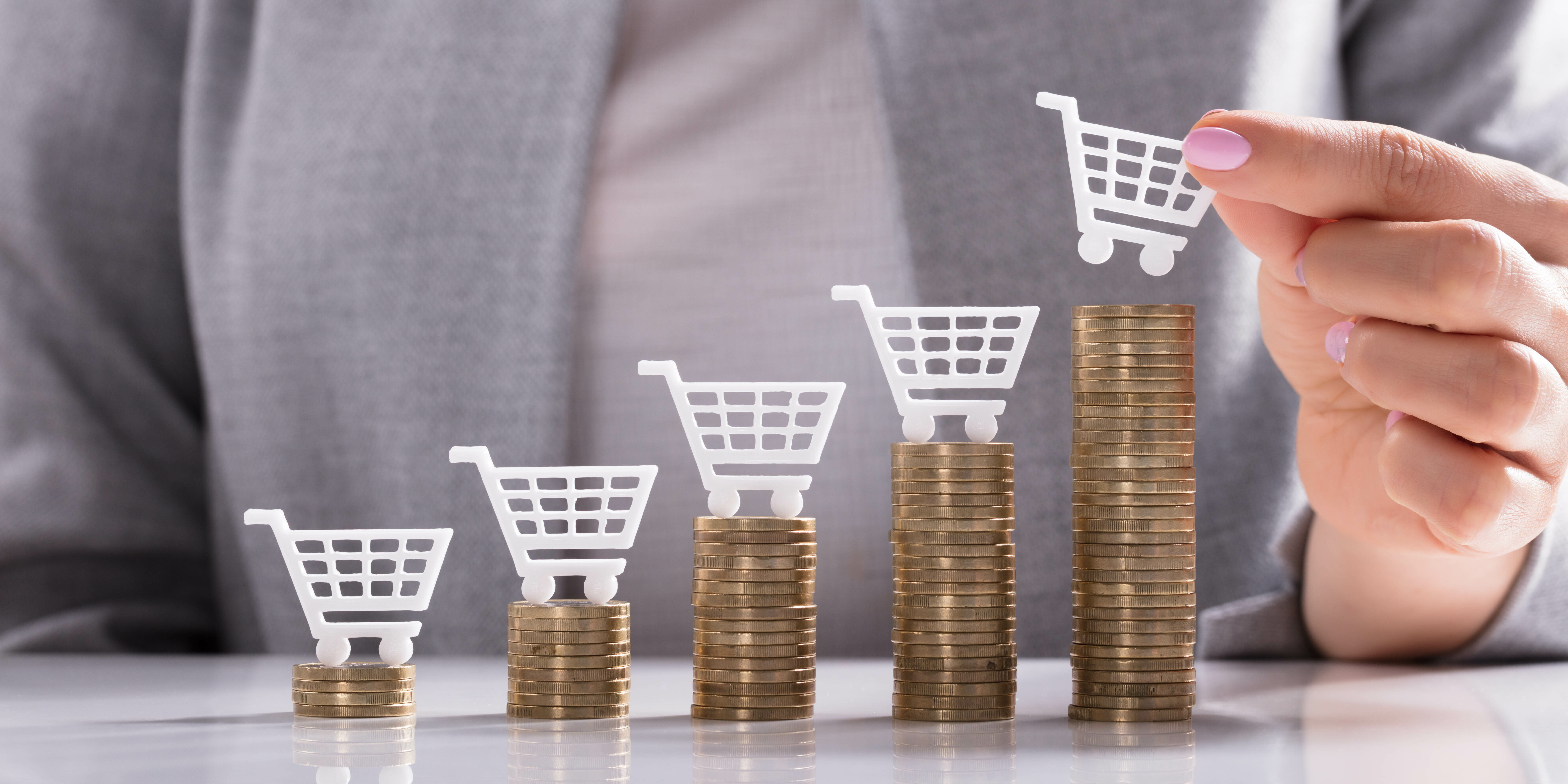 Businesswoman's Hand Placing White Shopping Cart On Top Of Golden Stacked Coins