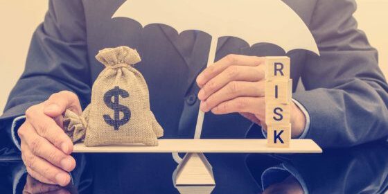 Financial risk assessment / portfolio risk management and protection concept : Businessman holds a white umbrella, protects a dollar bag on basic balance scale, defends money from being cheat or fraud