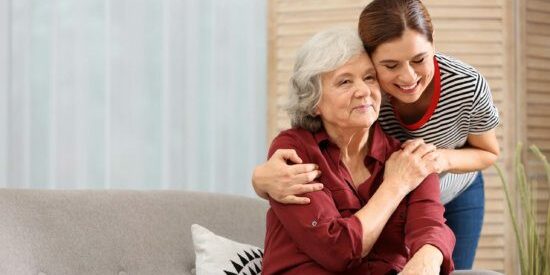 Elderly woman with female caregiver in living room. Space for text