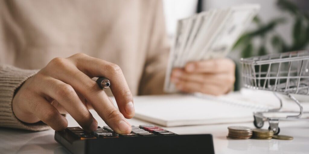 Woman counting and calculate cost money with calculator at home. Budget of disadvantaged and low income family for rising food and grocery store prices and expensive daily consumer goods concept.